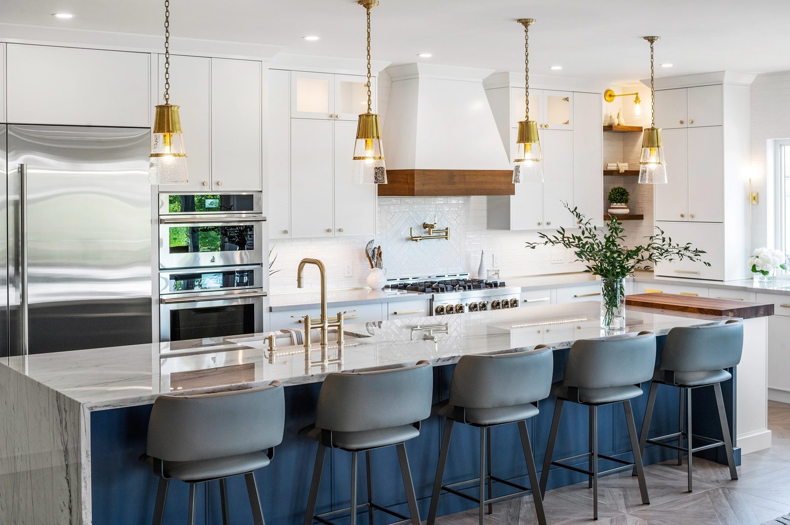 A white kitchen with a navy island and brass pendant lights